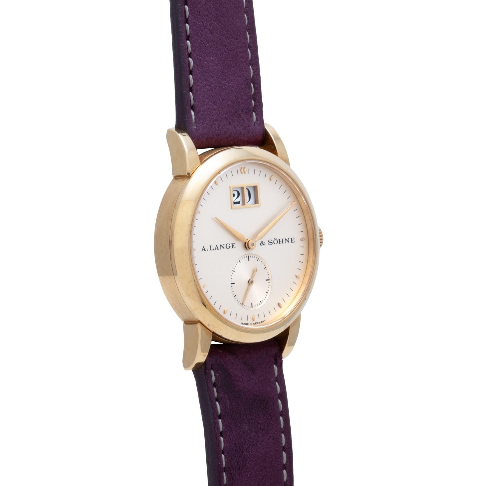 The Lange & Sohne Saxonia Outsize Date is a gold wristwatch featuring a white face, purple leather strap, and a prominent date display at 12 o’clock.