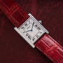 A Cartier Tank Louis watch with a red leather strap displayed on a dark red textured surface.