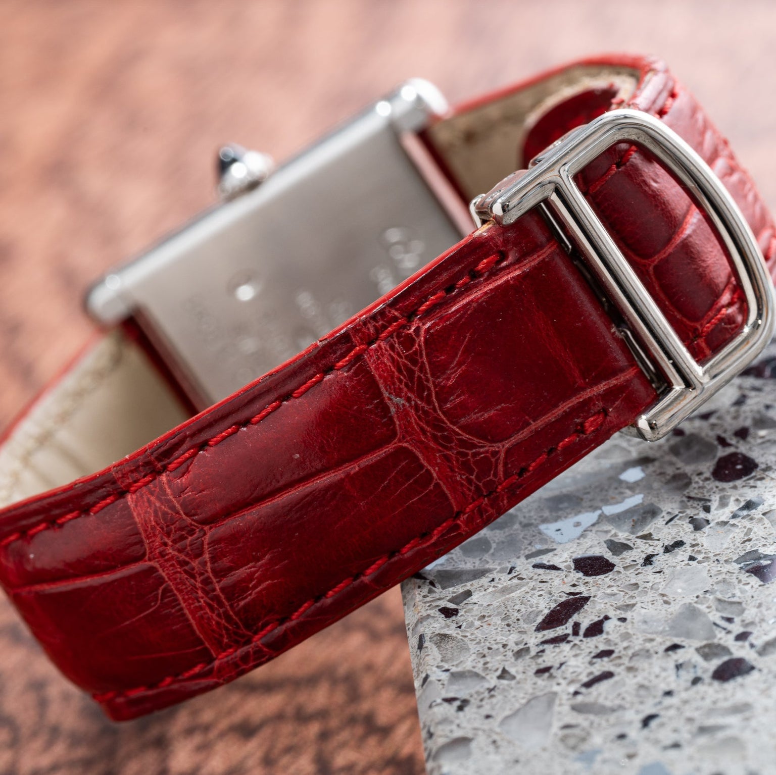Close-up of the Cartier Tank Louis red leather watch strap with a silver buckle, resting on a granite surface.