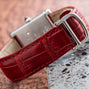 Close-up of the Cartier Tank Louis red leather watch strap with a silver buckle, resting on a granite surface.