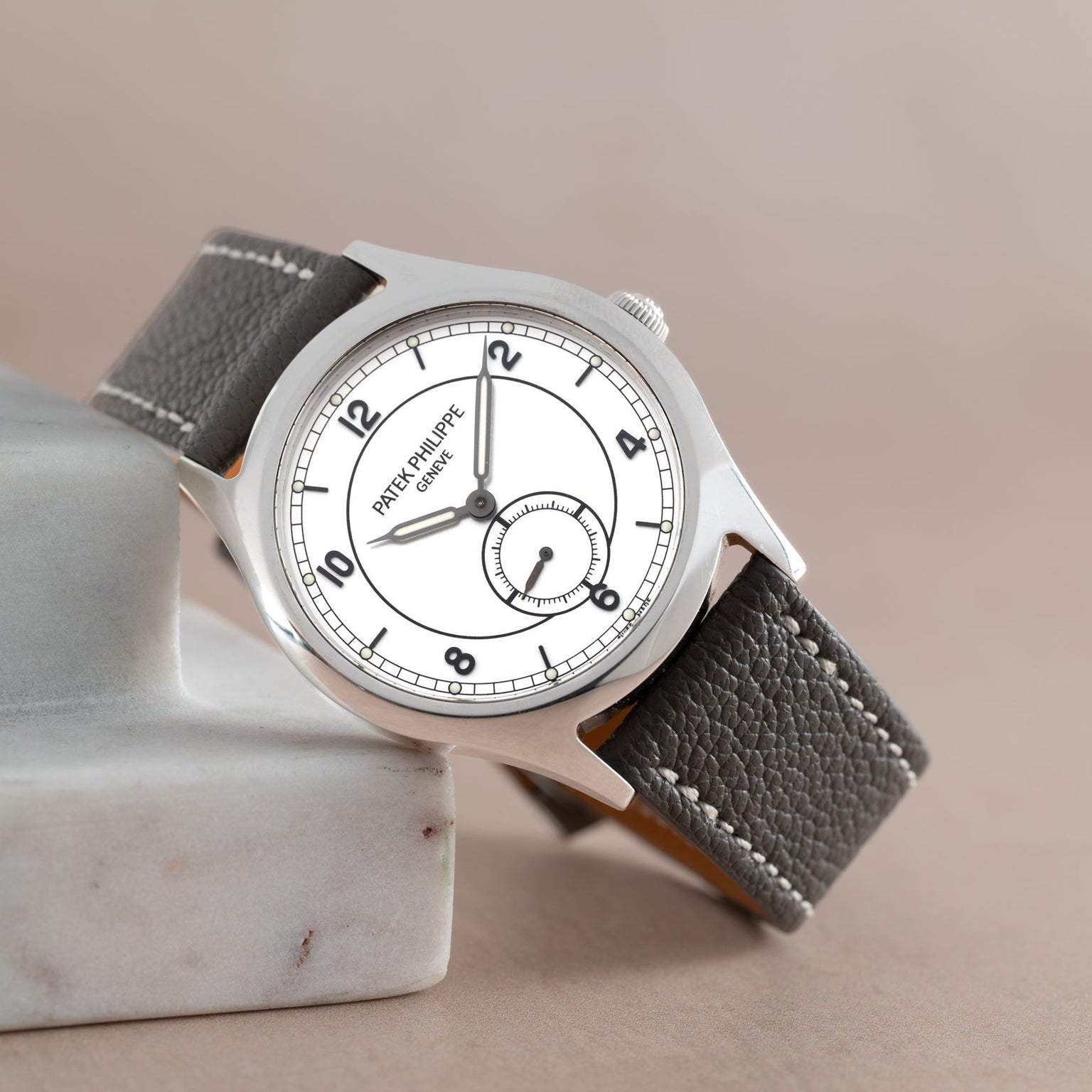 The Patek Philippe Calatrava Geneva Boutique Limited Edition wristwatch features a white dial and black leather strap, elegantly displayed on a marble block.
