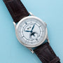 Patek Philippe Annual Calendar watch with white face, moonphase indicator, and dark brown leather strap displayed on a light blue background.