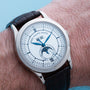 A close-up of a wrist wearing the Patek Philippe Annual Calendar watch, featuring a white dial and blue hands.