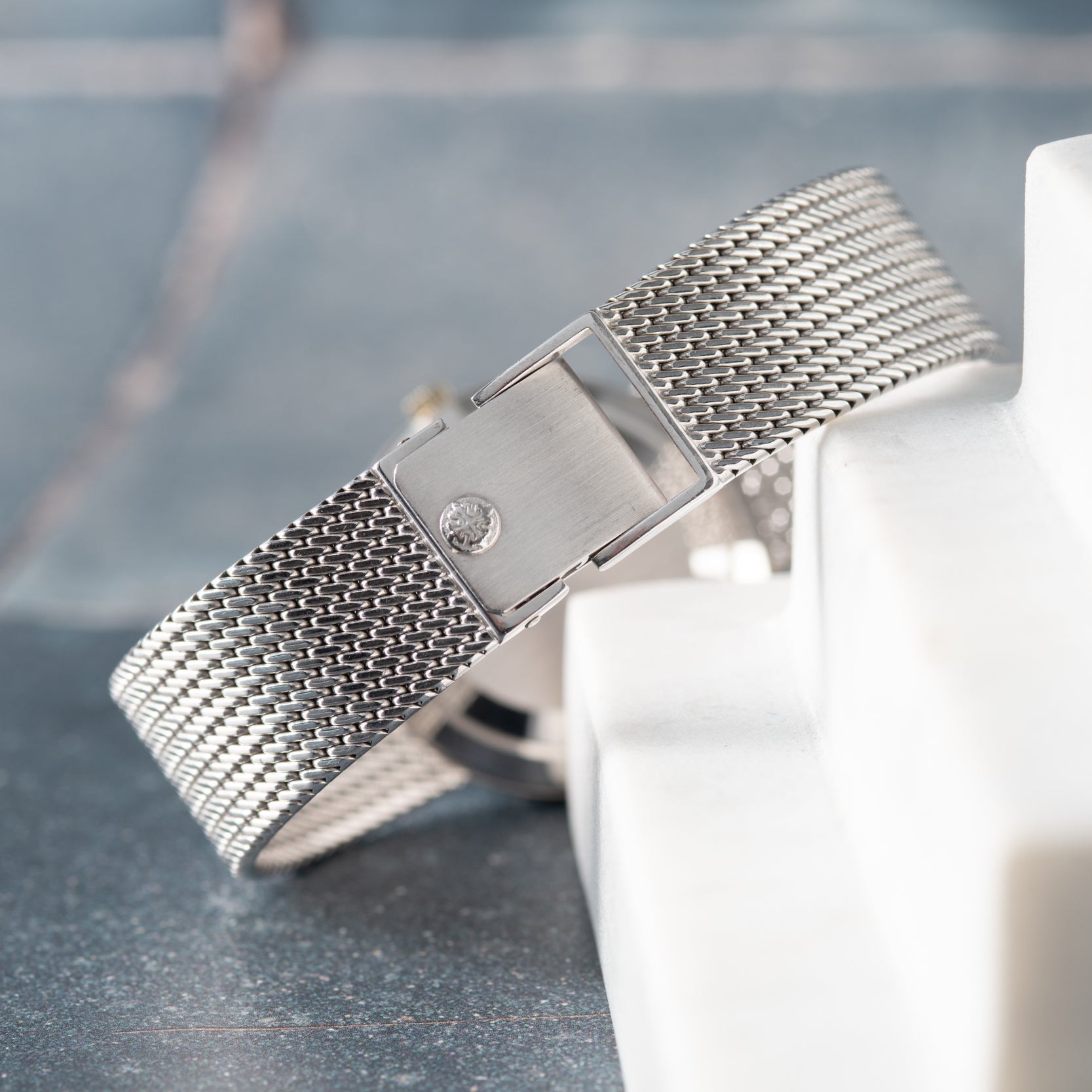 The Patek Philippe Calatrava features a silver mesh bracelet and a small diamond detail, elegantly displayed on a marble surface.