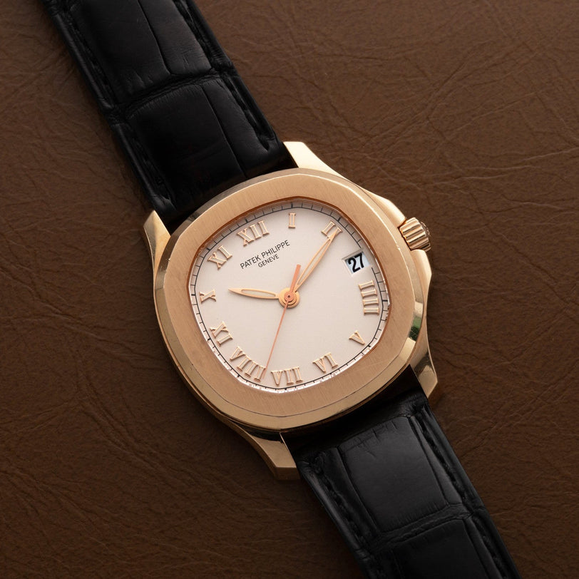 A Patek Philippe Aquanaut watch with Roman numerals and a black leather strap resting on a brown leather surface.