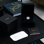 A Piaget Altiplano luxury watch in a black box sits next to a certificate, booklet, and book on a dark table.