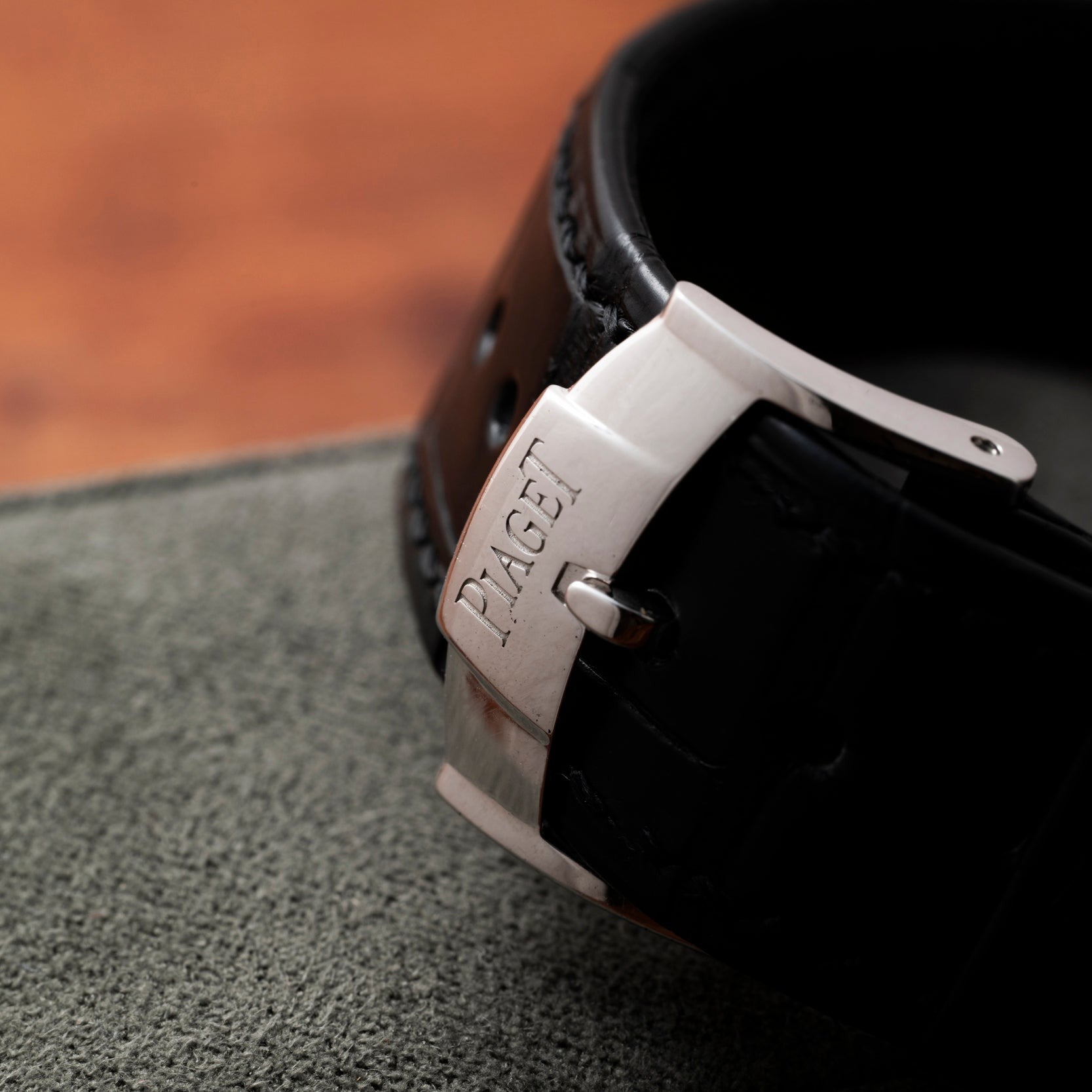 Close-up of a Piaget Altiplano watch buckle with a black leather strap on a gray surface.