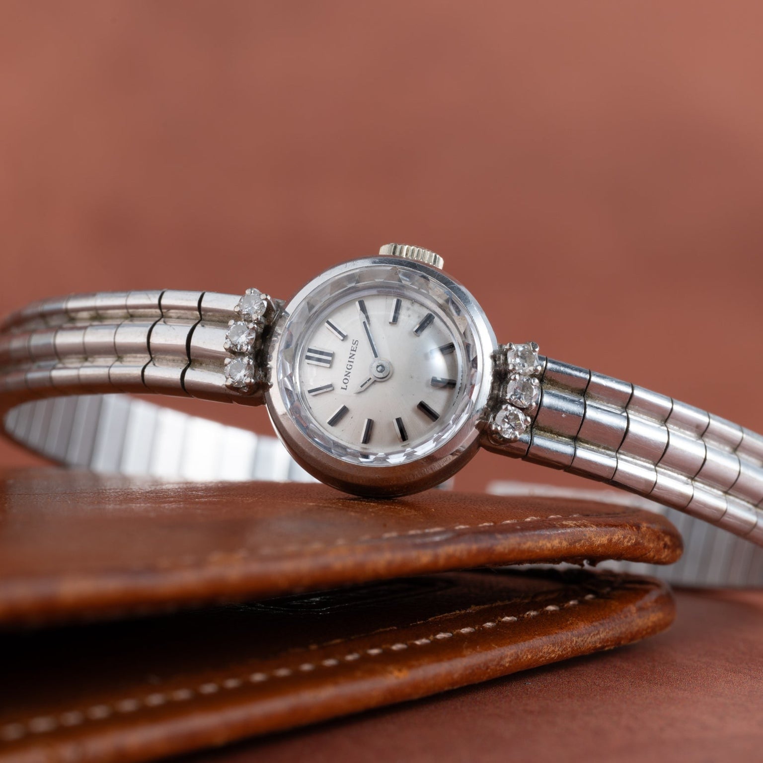A Longines Diamond Cocktail Watch for women, featuring diamond accents, rests atop a brown leather wallet.