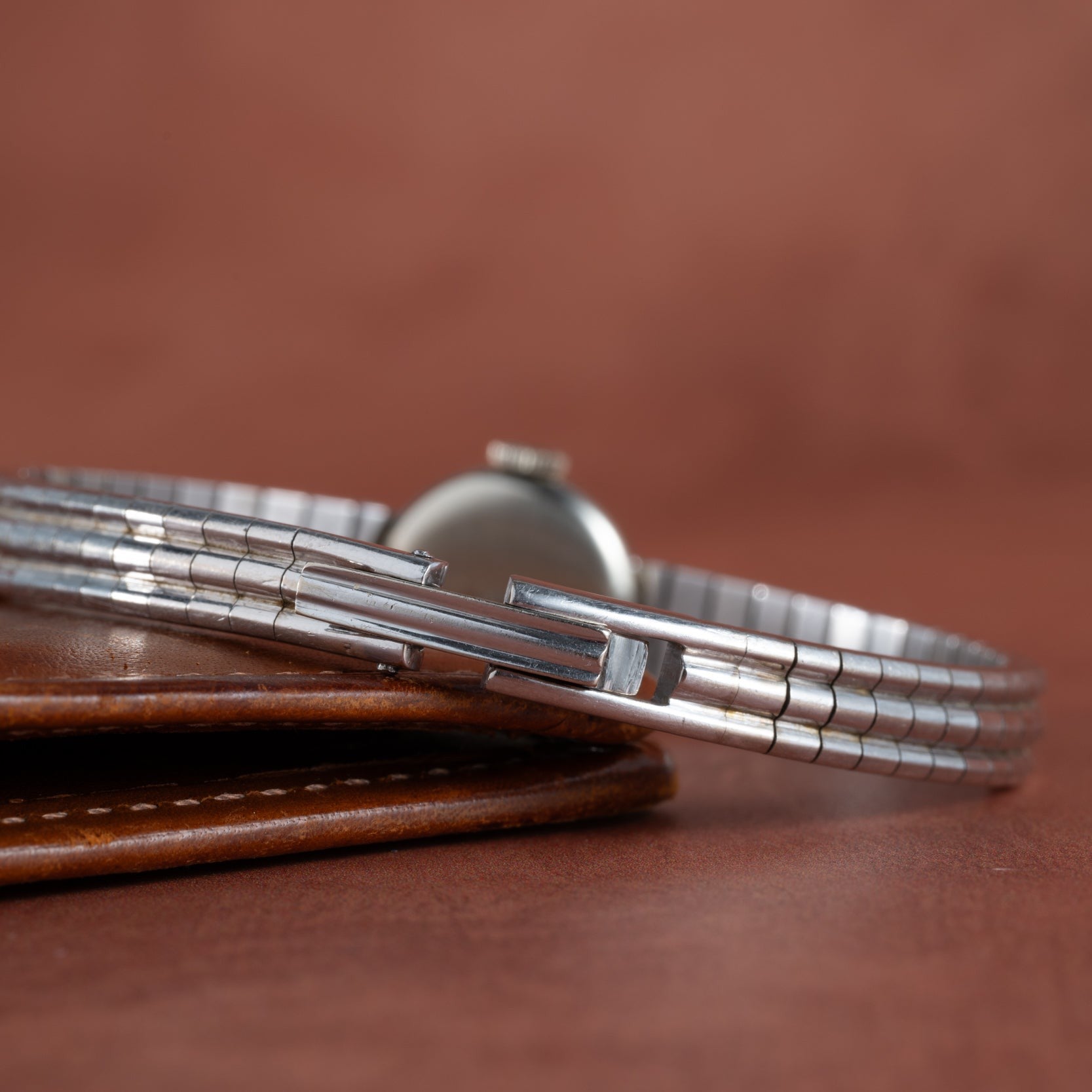 The Longines Diamond Cocktail Watch with a metal band sits atop a brown leather wallet against a brown background.