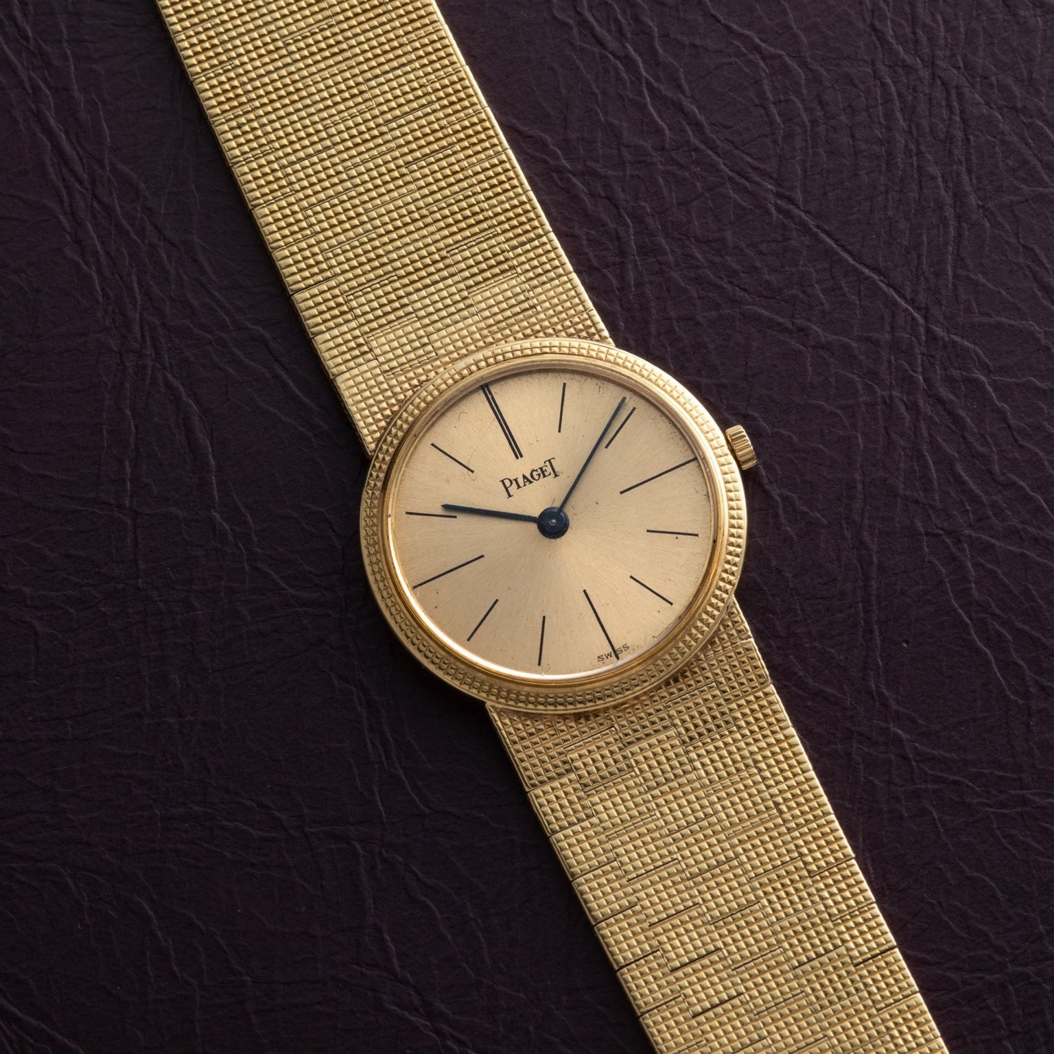 18K Yellow Gold Dress Watch by Piaget with a textured band displayed on a dark leather surface.