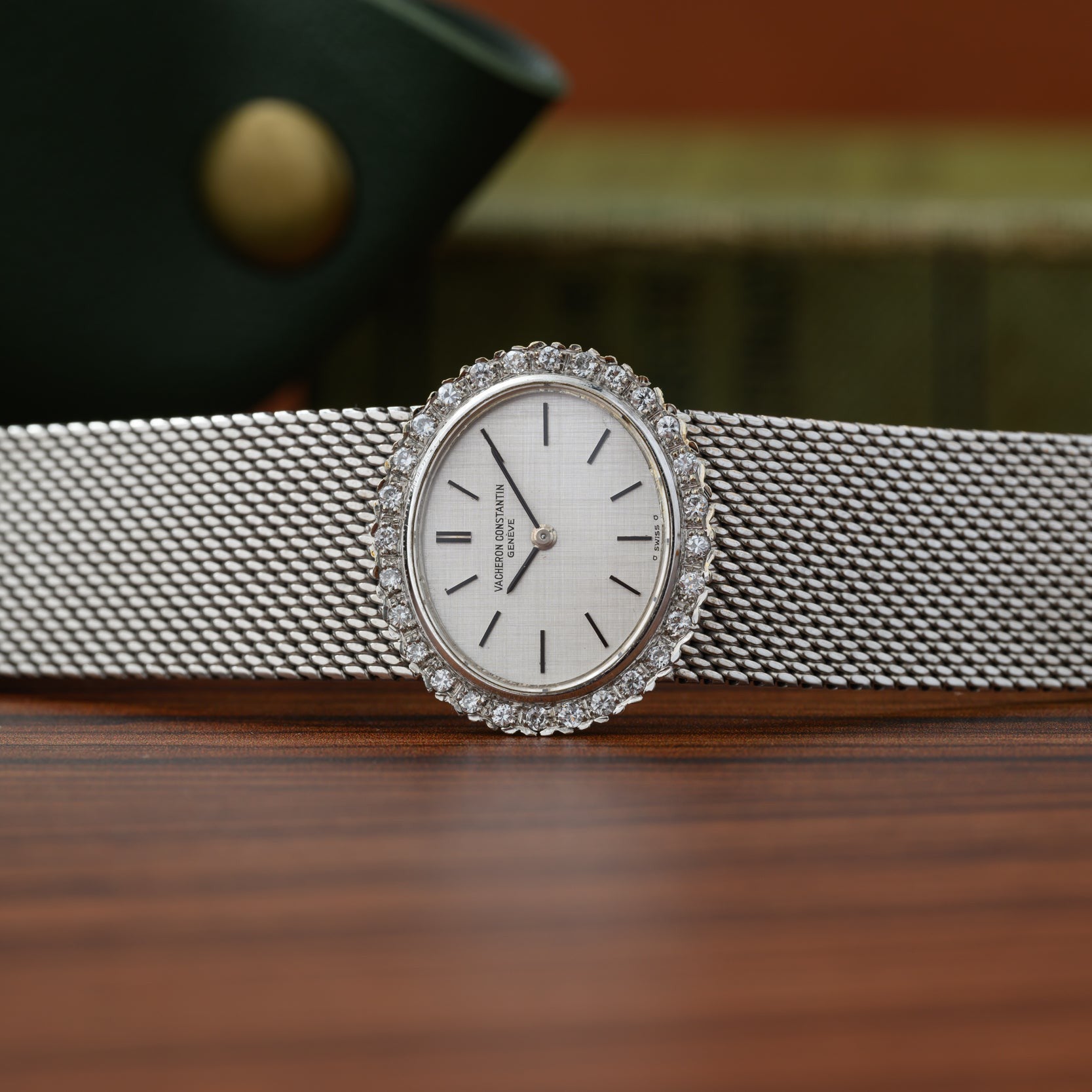 Vacheron Constantin White Gold Diamond Bezel watch with a mesh band displayed on a wooden surface, with books in the background.