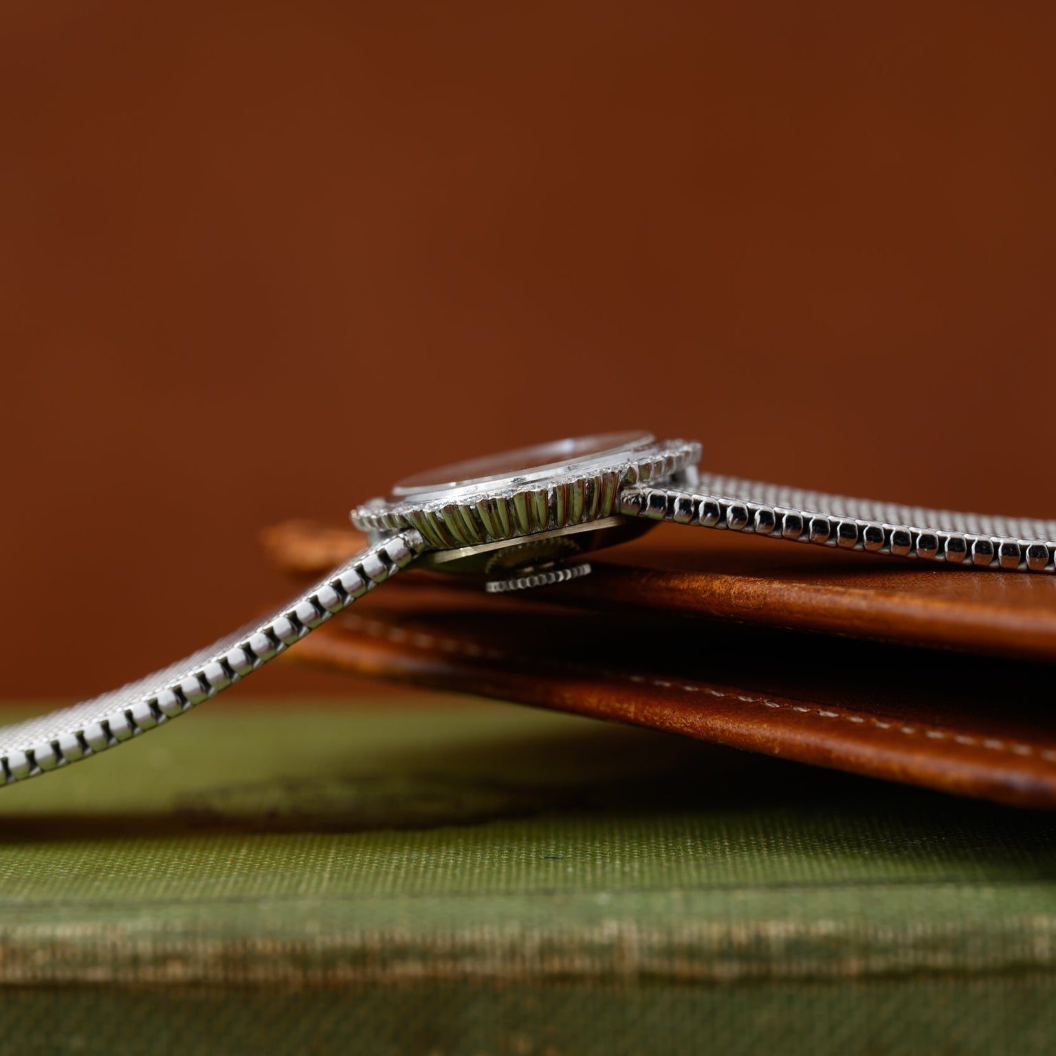 A Vacheron Constantin White Gold Diamond Bezel wristwatch with a metal band rests on a brown leather wallet and a green book.