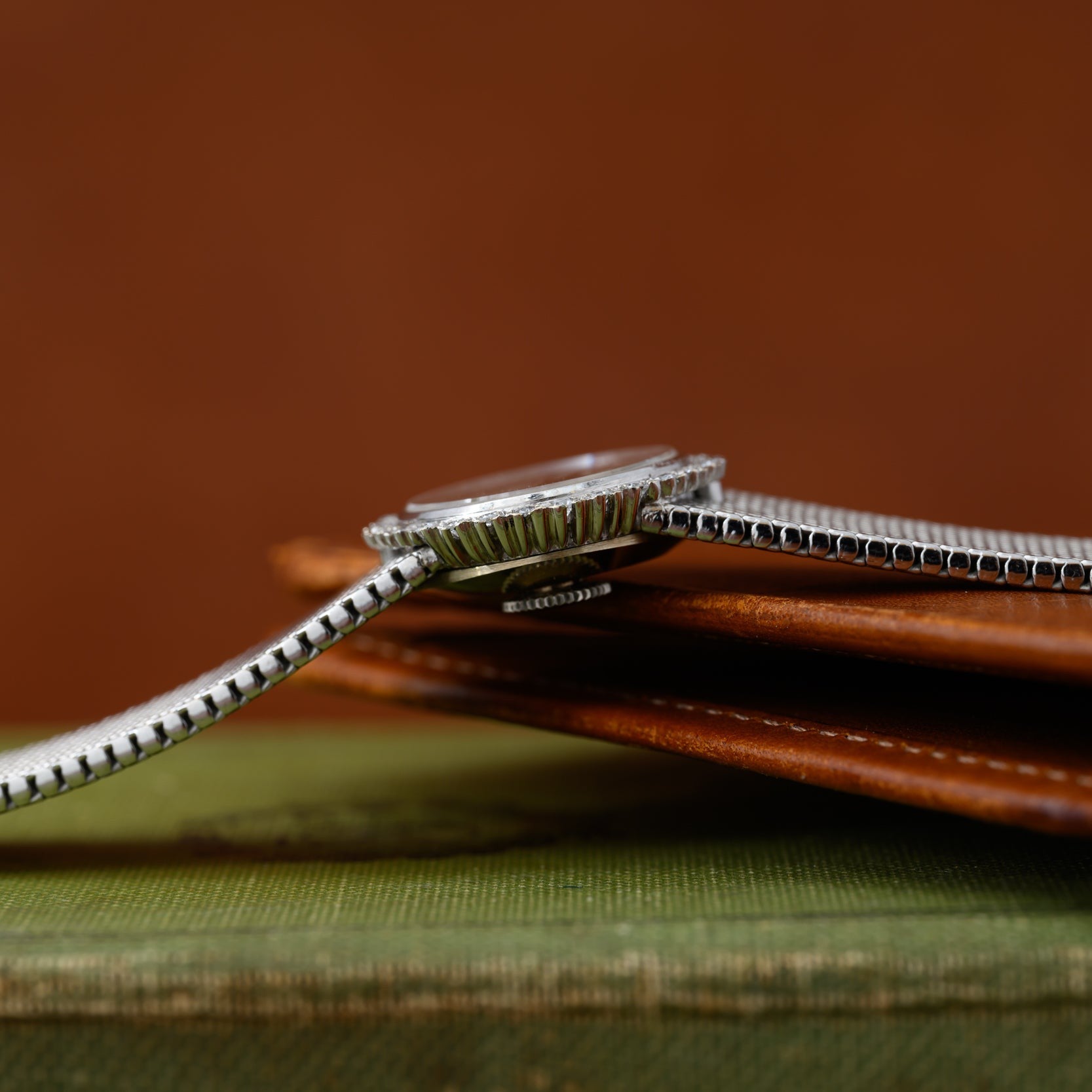 A Vacheron Constantin White Gold Diamond Bezel wristwatch with a metal band rests on a brown leather wallet and a green book.