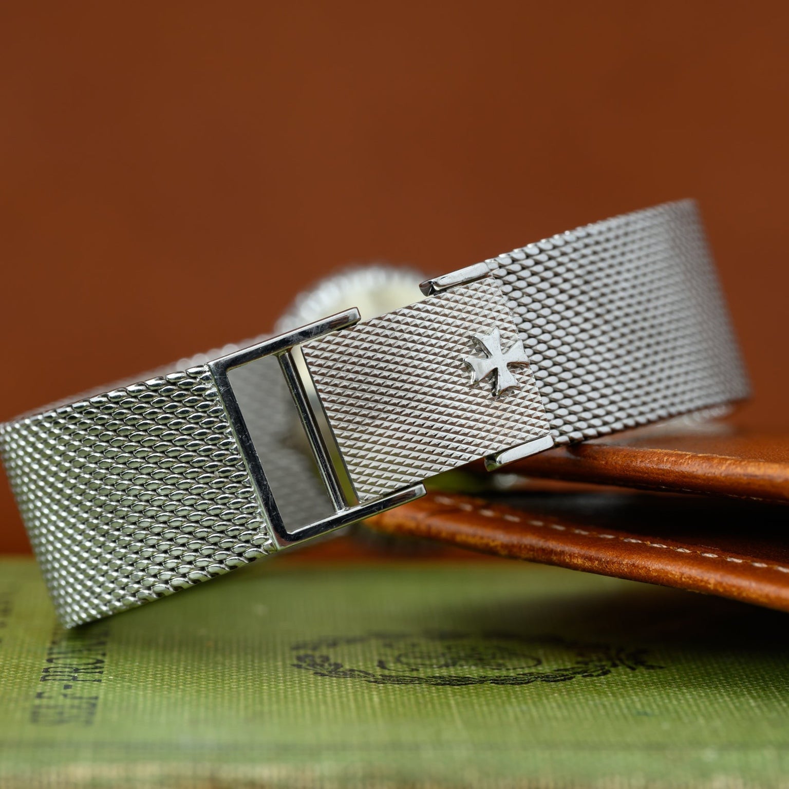 A close-up of a Vacheron Constantin White Gold Diamond Bezel watch bracelet with an engraved cross emblem, resting on a green book.