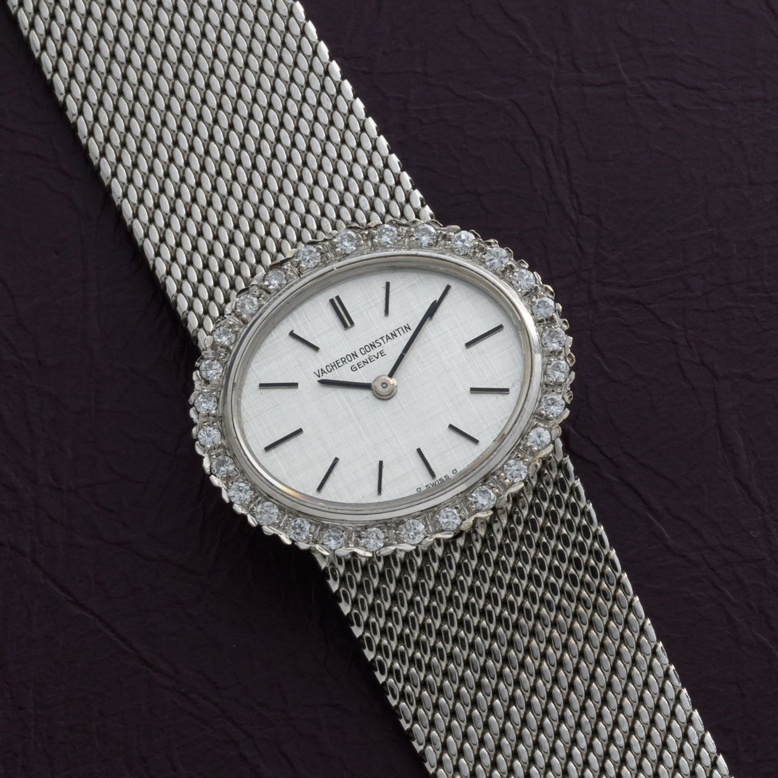 A Vacheron Constantin White Gold Diamond Bezel watch is shown on a mesh band, resting on a dark textured surface.