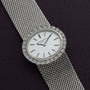 A Vacheron Constantin White Gold Diamond Bezel watch is shown on a mesh band, resting on a dark textured surface.