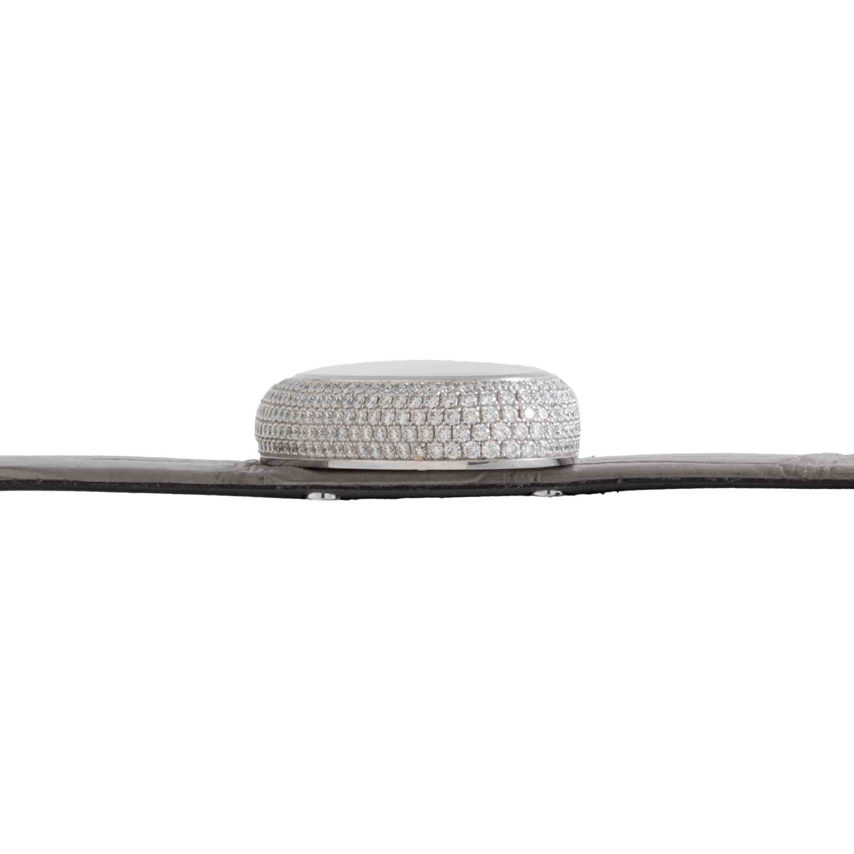 Side view of Cartier’s Libre Hypnose, a round silver object encrusted with diamonds, placed on a flat dark surface against a white background.