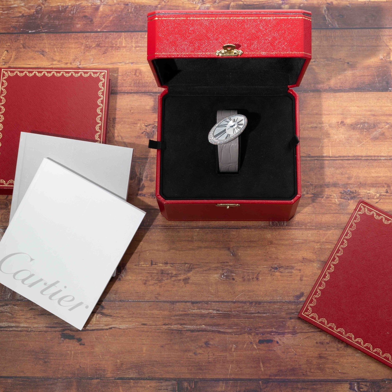 A Cartier Libre Hypnose watch displayed in a red box with booklets on a wooden surface.