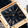 Close-up of the Cartier Santos Dumont gold wristwatch featuring a black face and Roman numeral hour markers.