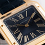 Close-up of a Cartier Santos Dumont watch face featuring gold Roman numerals on a black background.