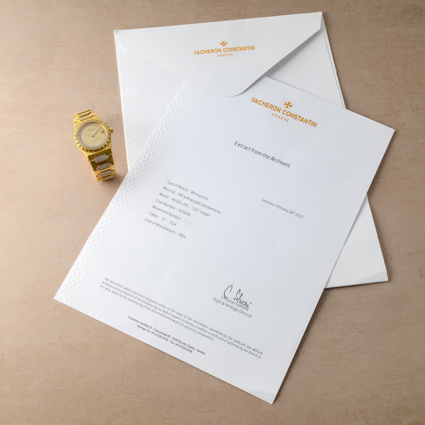 A Vacheron Constantin 222 gold wristwatch, a white envelope, and an official Vacheron Constantin document rest on a beige surface.
