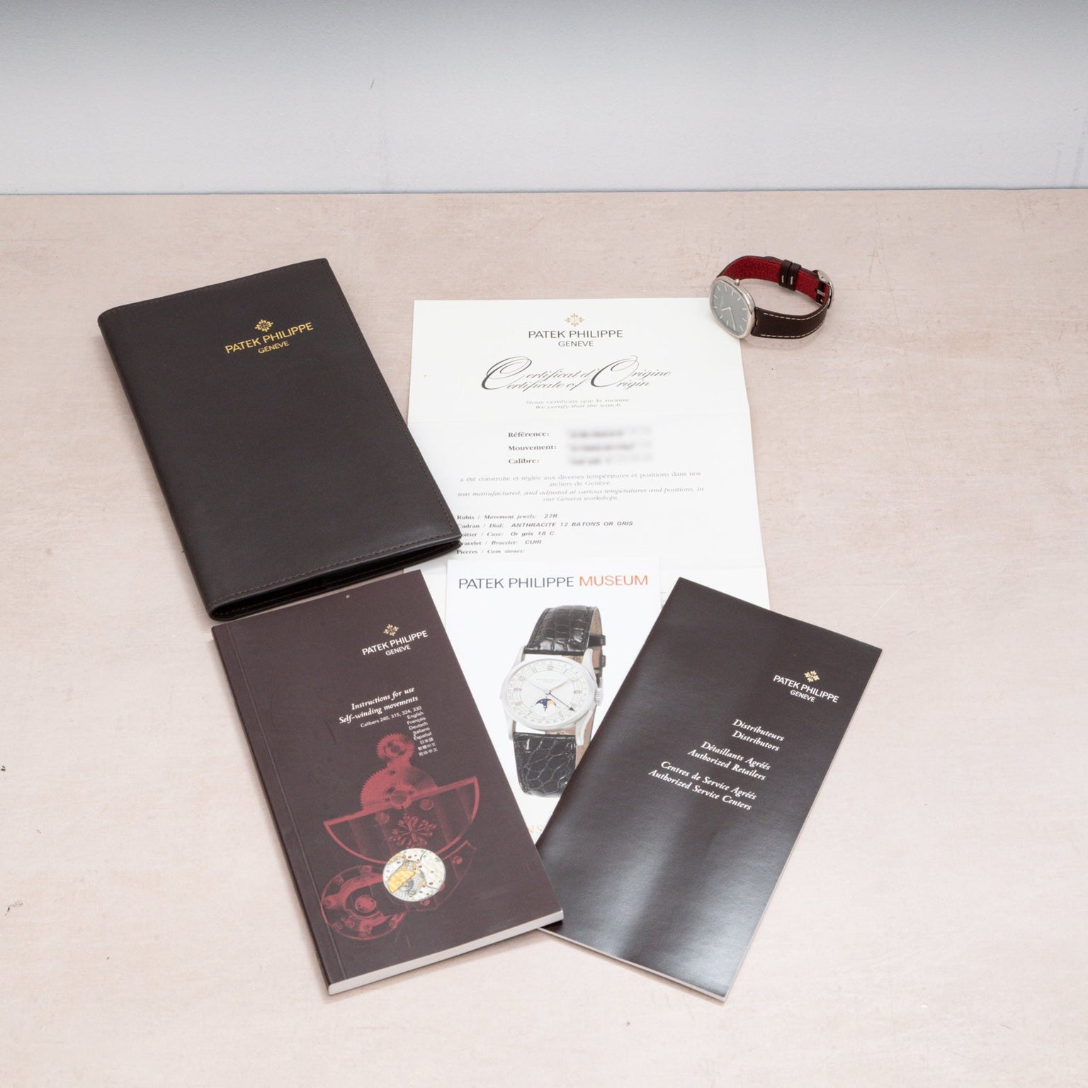 Patek Philippe Ellipse watch with certificate, manuals, brochure, and black folder displayed on a beige surface.