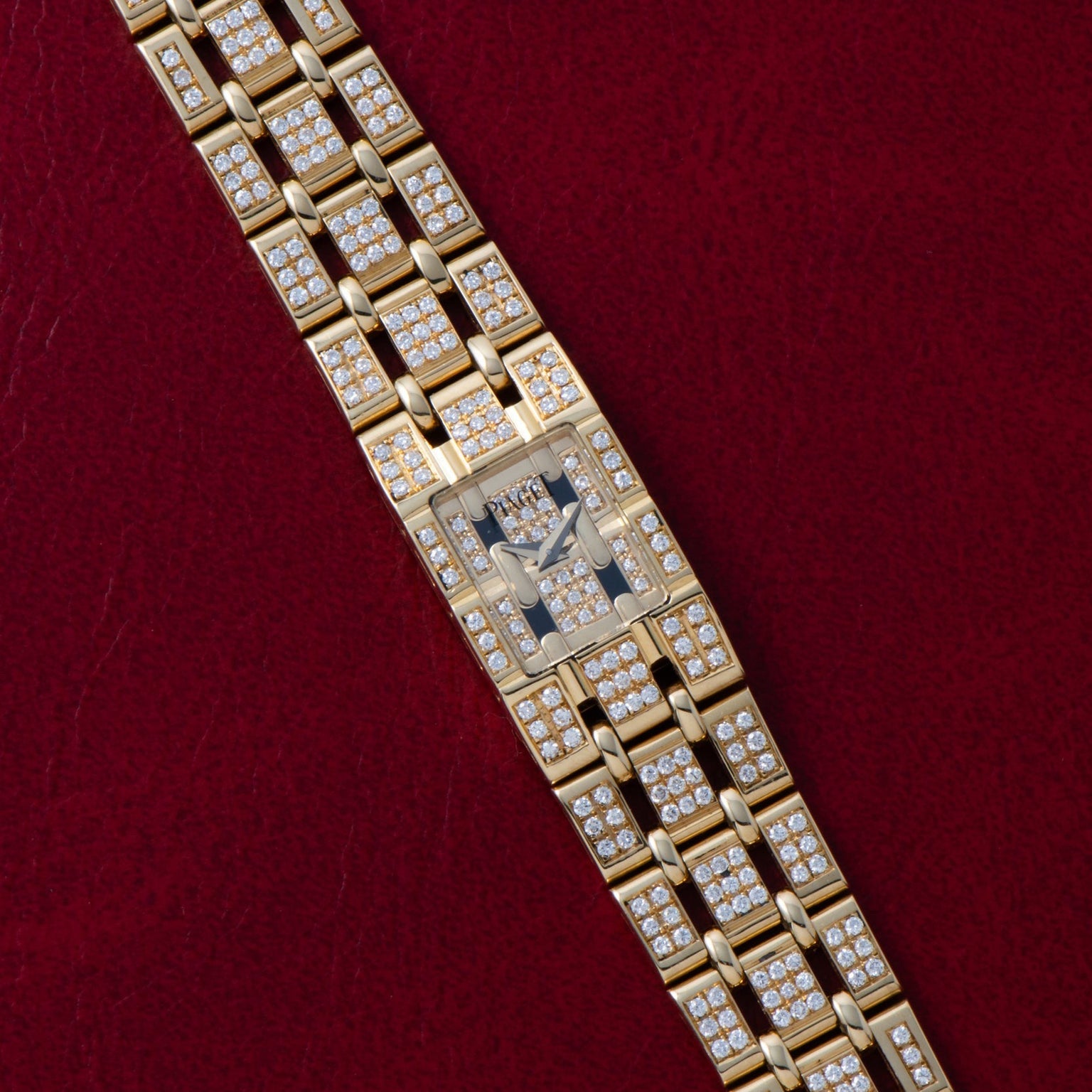 Piaget Polo Pave diamond-encrusted gold wristwatch displayed on a red textured background.