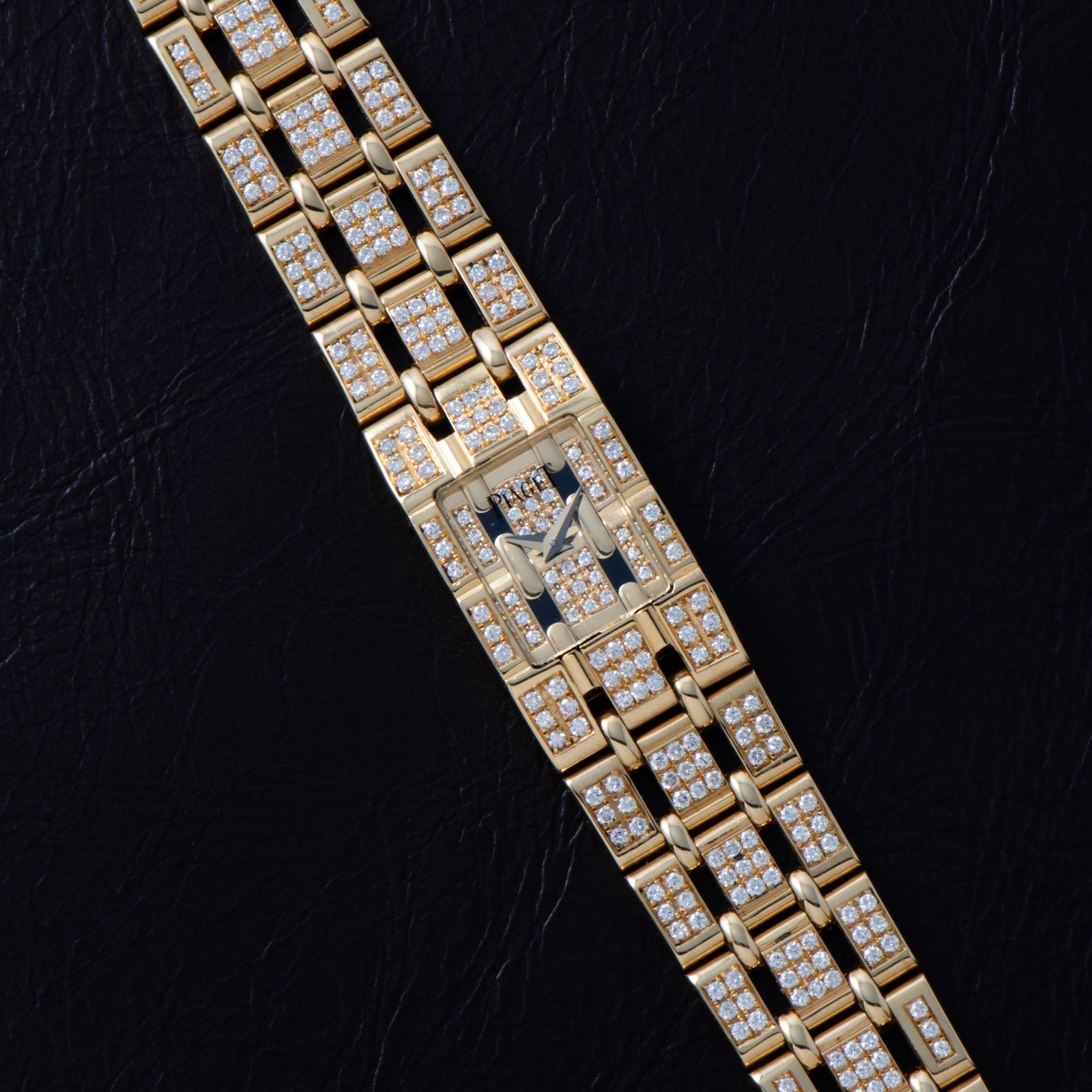 The Piaget Polo Pave, a gold wristwatch with a rectangular face and diamond accents, is showcased on a black leather surface.