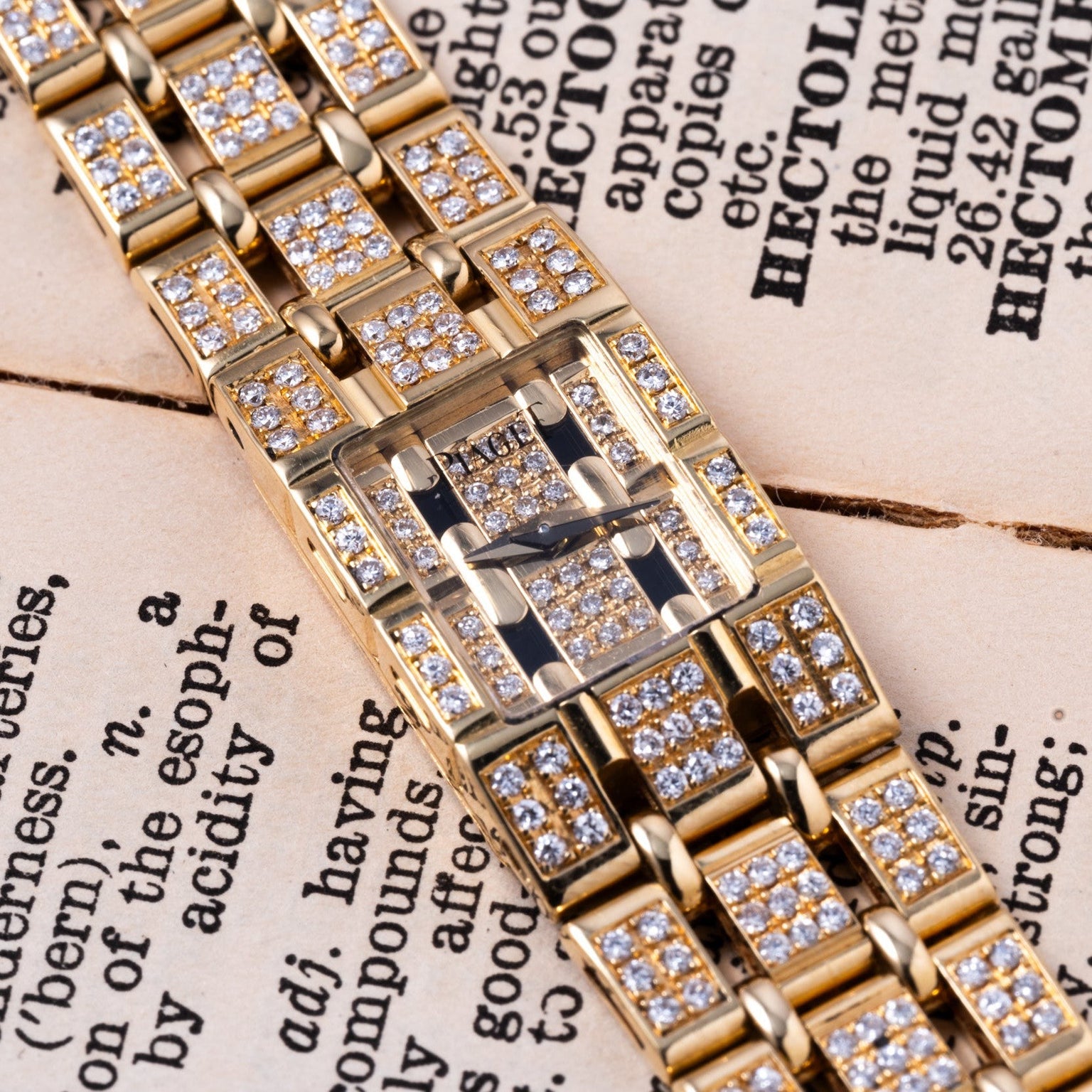 The Piaget Polo Pave, a gold and diamond-encrusted wristwatch, is elegantly displayed atop an open book with visible text.