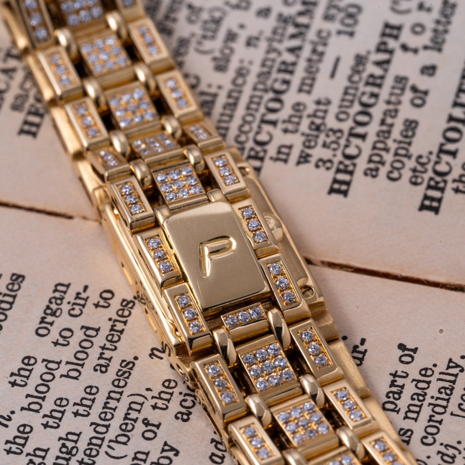 Close-up of the Piaget Polo Pave gold and diamond watch bracelet resting on an open book with visible text.