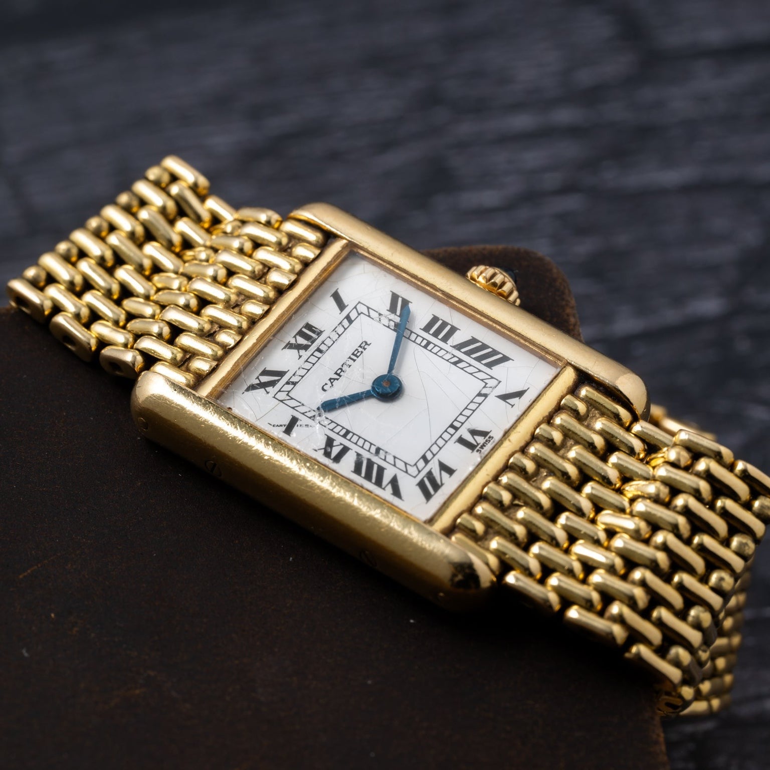 Cartier Tank Louis wristwatch with Roman numerals on a white dial, shown on a dark textured surface.