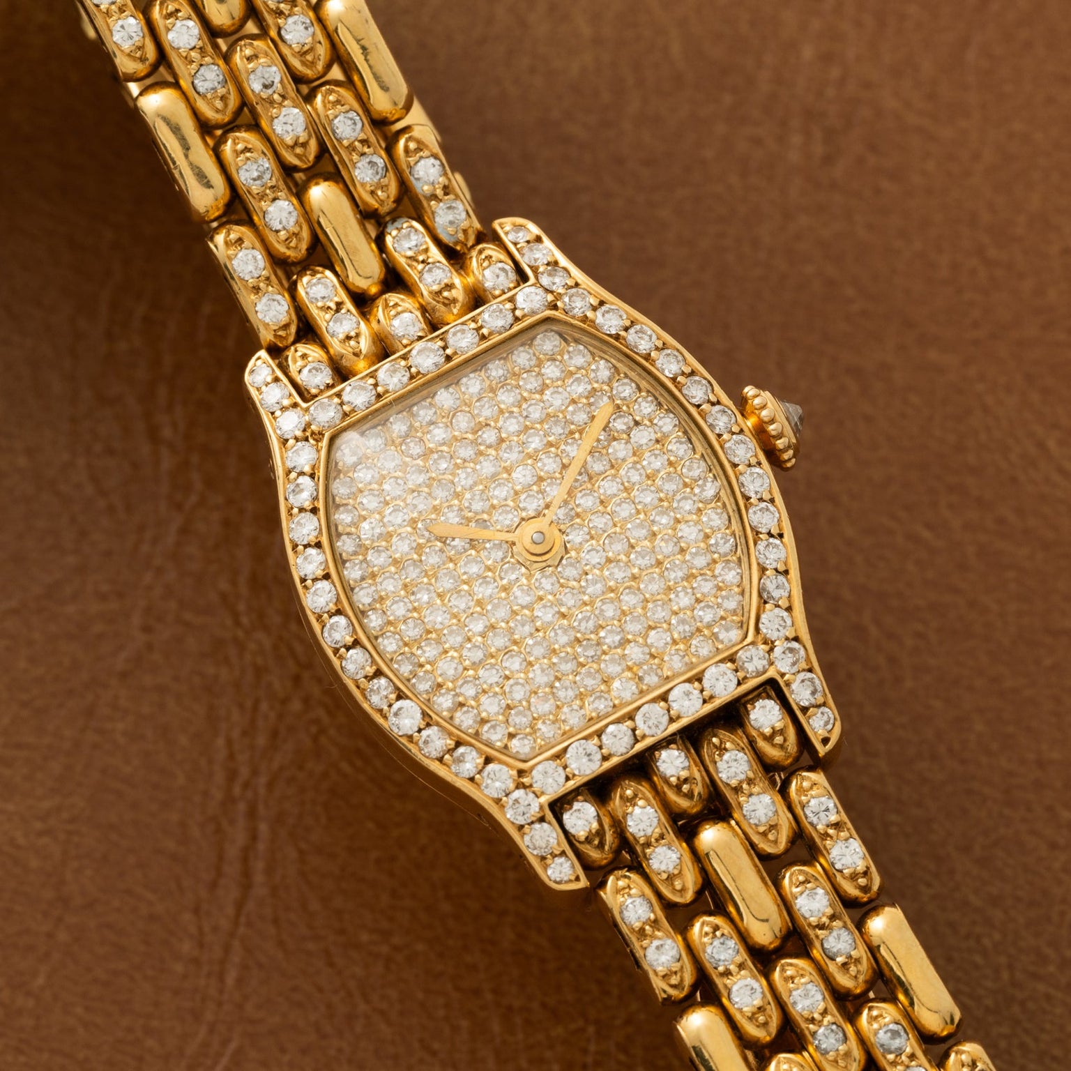 Cartier Tortue Diamond watch featuring a diamond-studded face and bracelet, displayed on a brown leather surface.