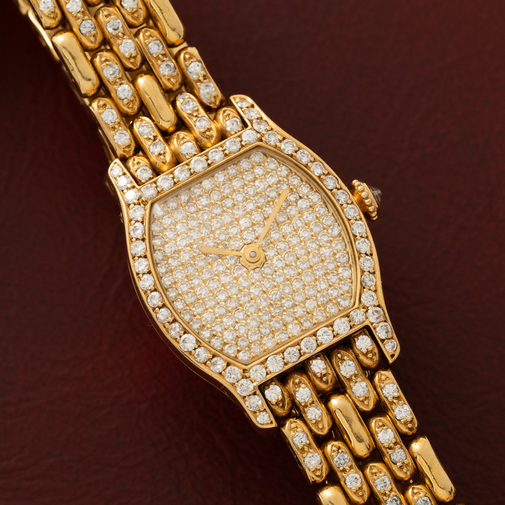 The Cartier Tortue Diamond wristwatch, adorned with diamonds, is showcased against a dark reddish-brown background.