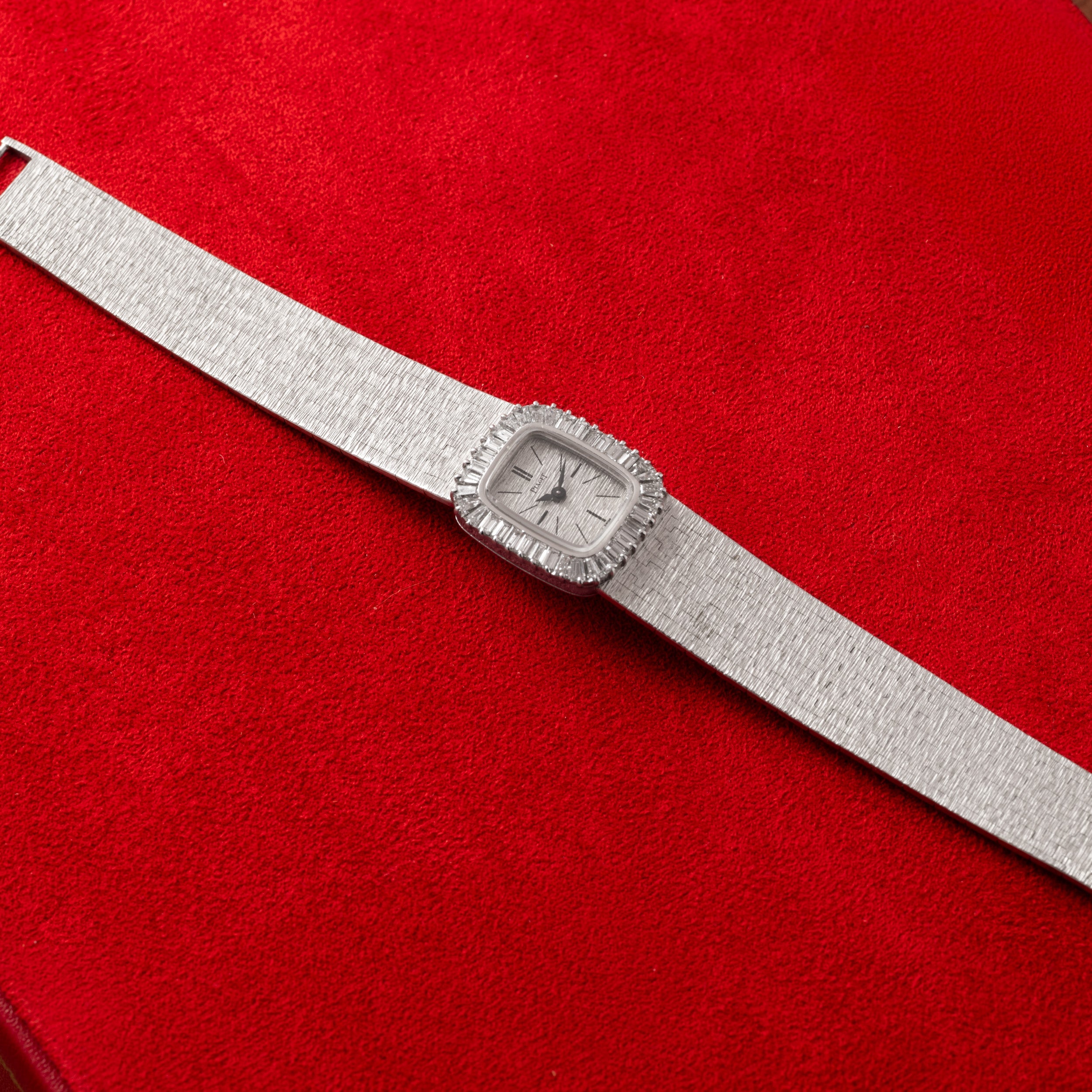 A Piaget White Gold Bark Diamond Dress Watch with a rectangular face rests on a red textured surface.