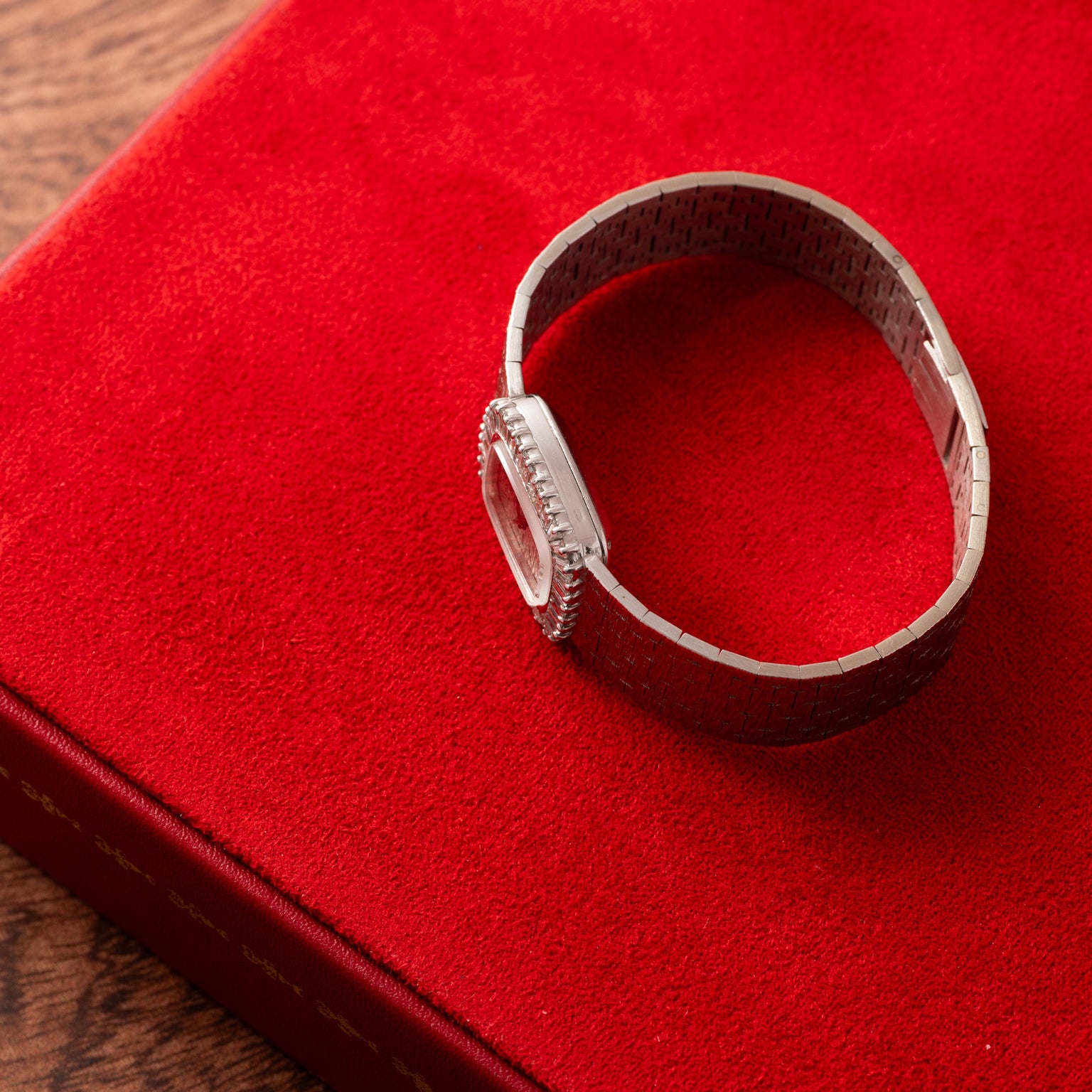 A Piaget White Gold Bark Diamond Dress Watch with a metal band rests on a red velvet surface.
