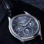 The Patek Philippe Perpetual Calendar wristwatch features a black face with multiple dials and a black leather strap.