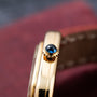 Close-up of the Cartier Gondole Ladies gold watch crown with a blue gemstone, featuring a brown leather strap in the background.