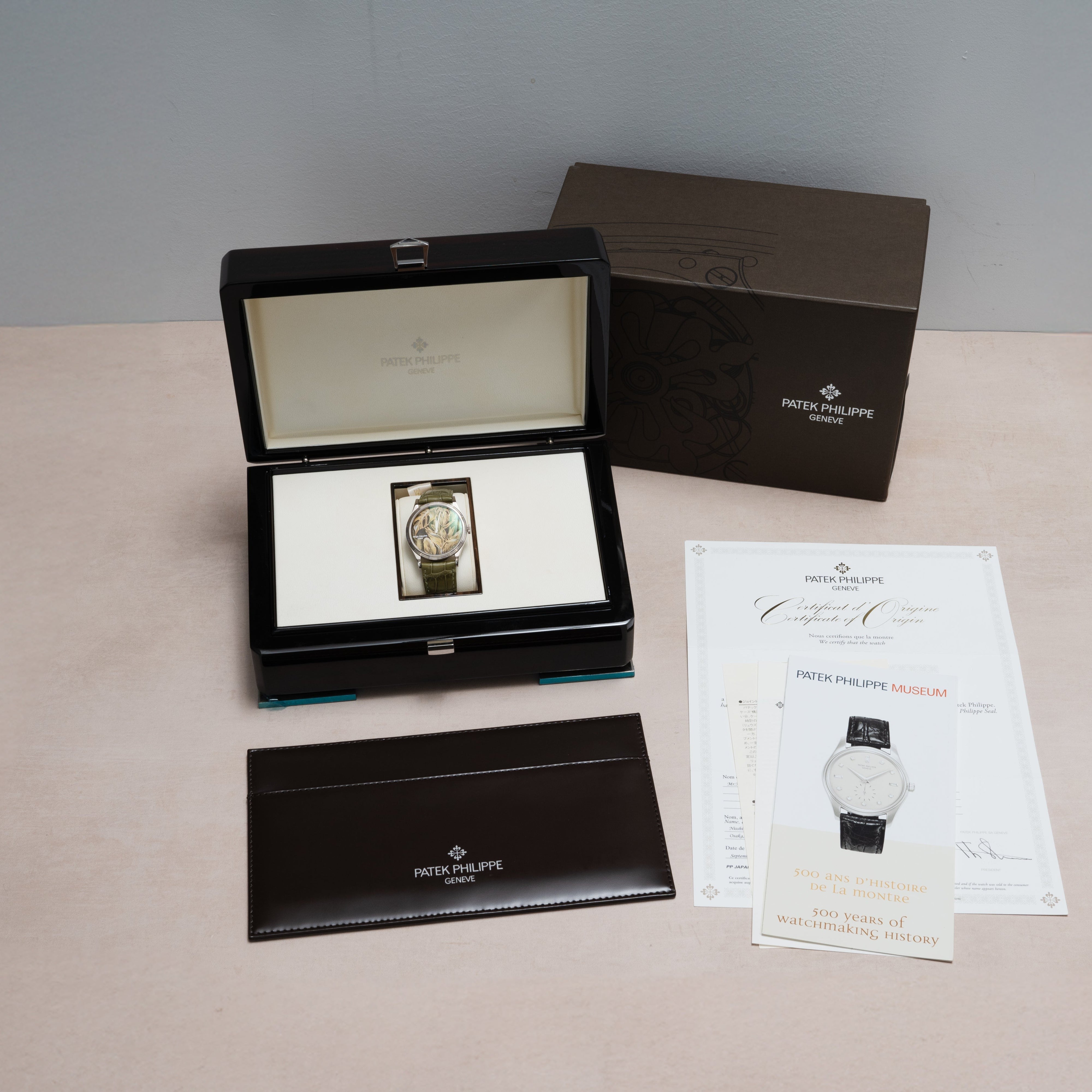 A Patek Philippe Calatrava Cloisonné Tropical Leaves II watch in its box, with papers, booklet, and outer packaging displayed on a light surface.