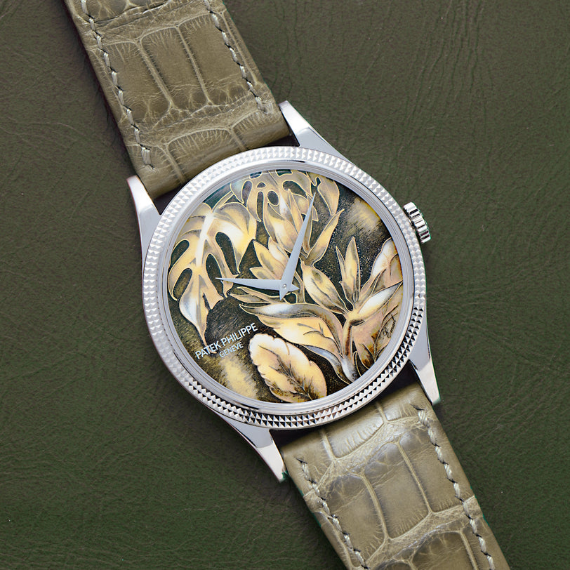 The Patek Philippe Calatrava Cloisonné Tropical Leaves II is a luxury watch with a green leather strap and an intricate leaf-patterned dial in earthy tones.