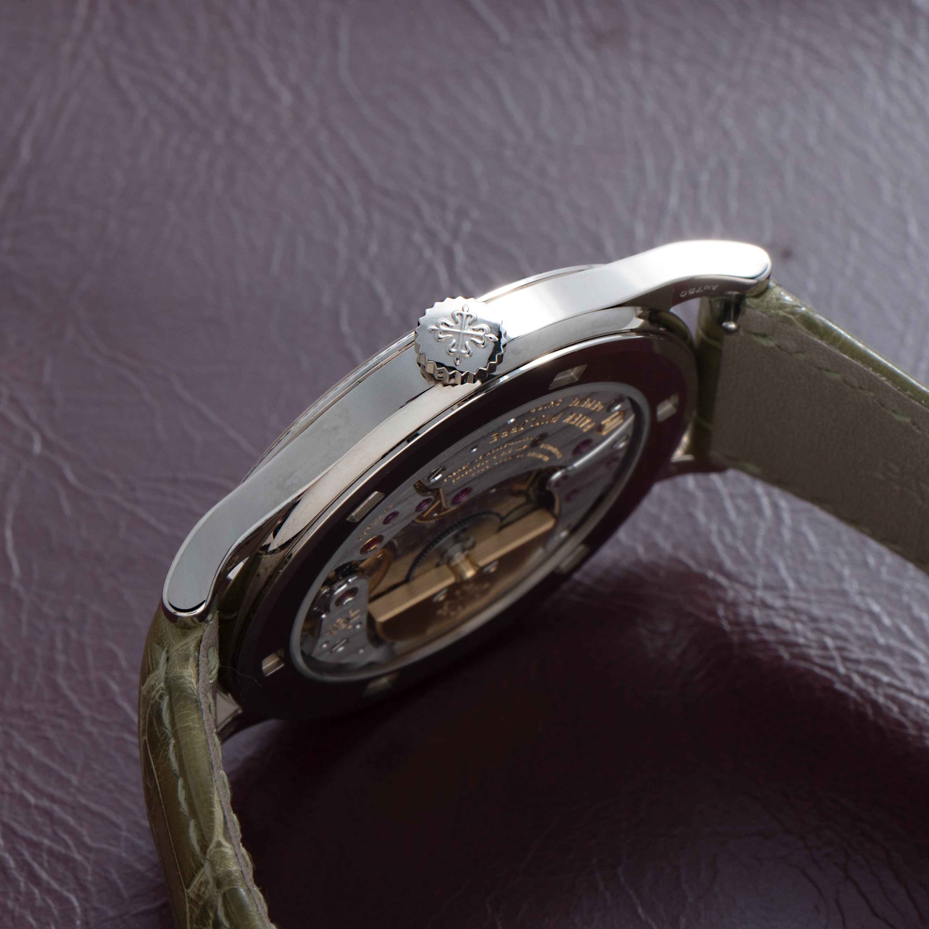 Close-up side view of the Patek Philippe Calatrava Cloisonné Tropical Leaves II luxury watch with a green strap on a textured brown surface.