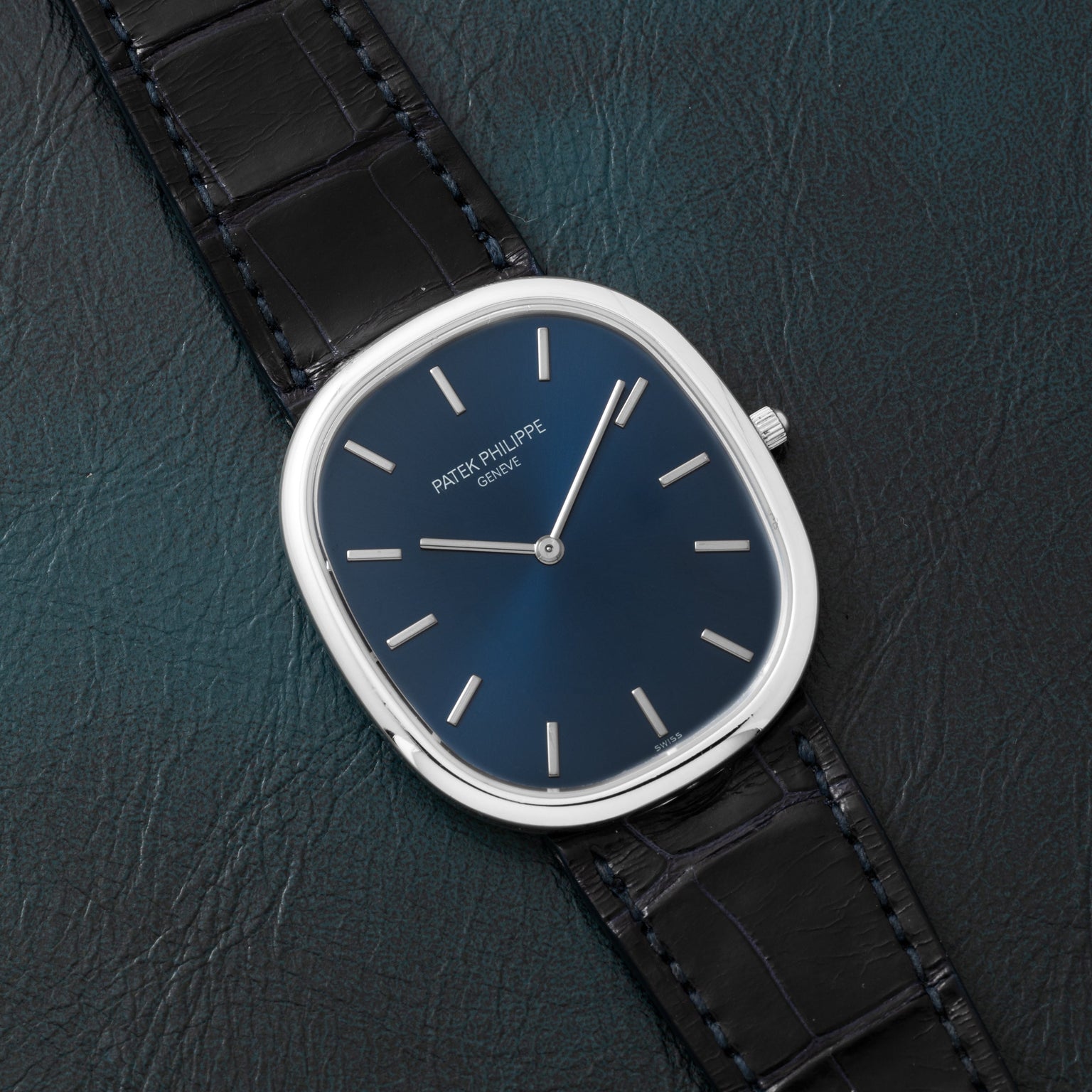 A Patek Philippe Ellipse Jumbo watch with a blue face and black leather strap rests on a dark textured surface.