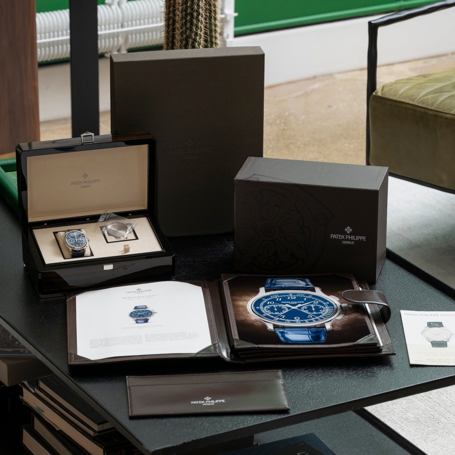 A Patek Philippe Split-Seconds Chronograph watch with its box, documents, and accessories is displayed on a black table.