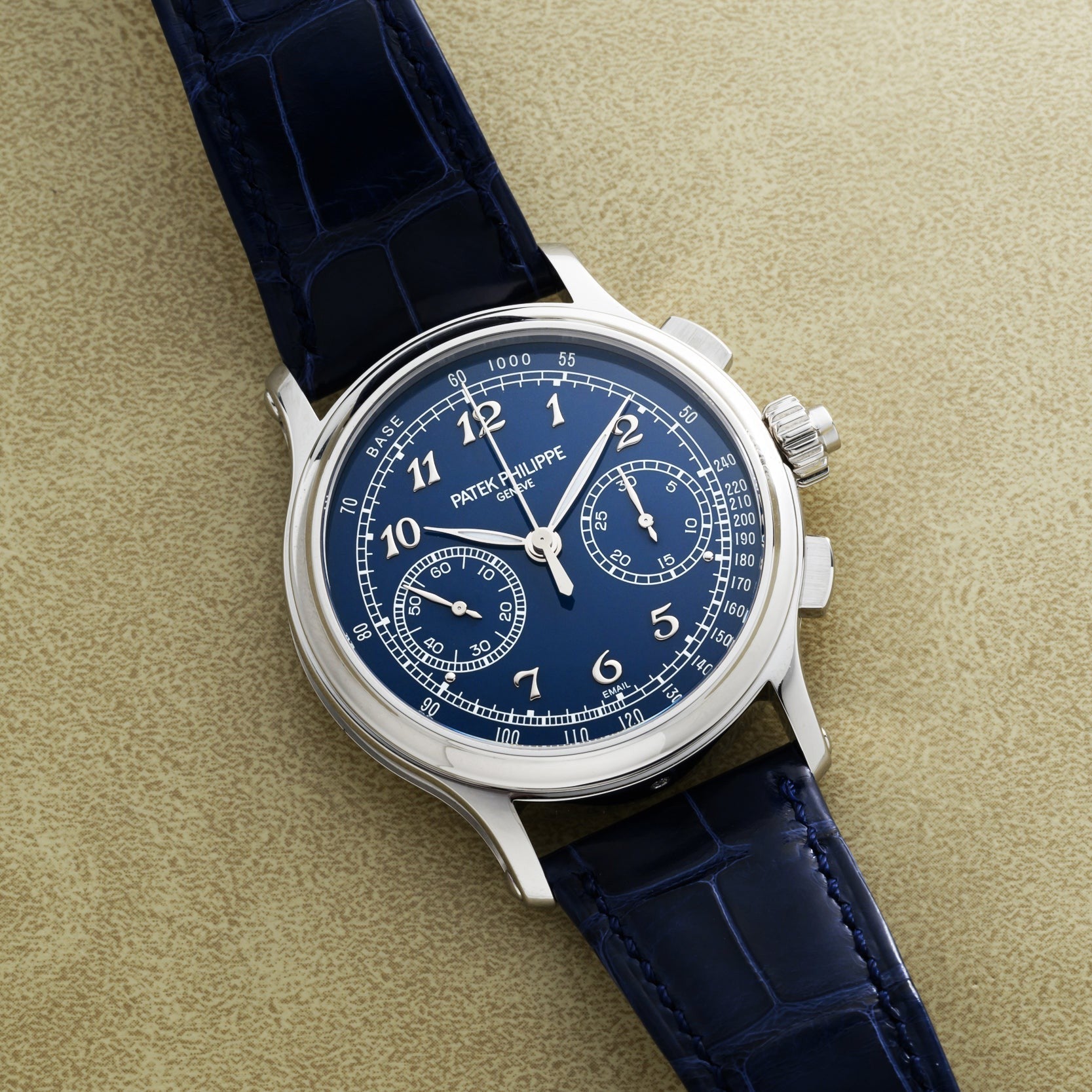 A Patek Philippe Split-Seconds Chronograph featuring a blue dial and blue leather strap, displayed on a tan textured surface.