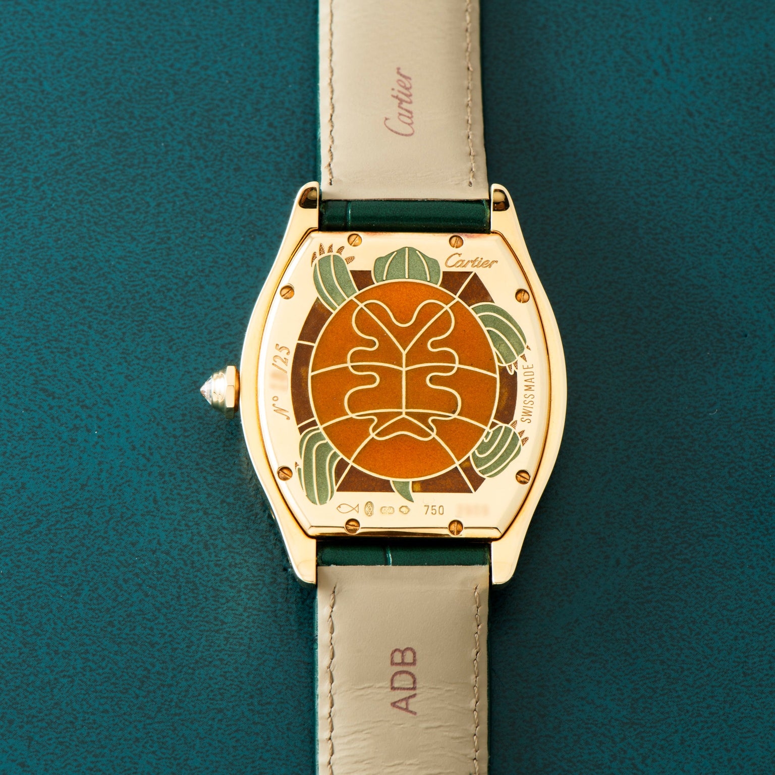 Cartier Tortue XL Turtle Limited Edition wristwatch with a leaf and plant motif engraved on the back, displayed on a green surface.