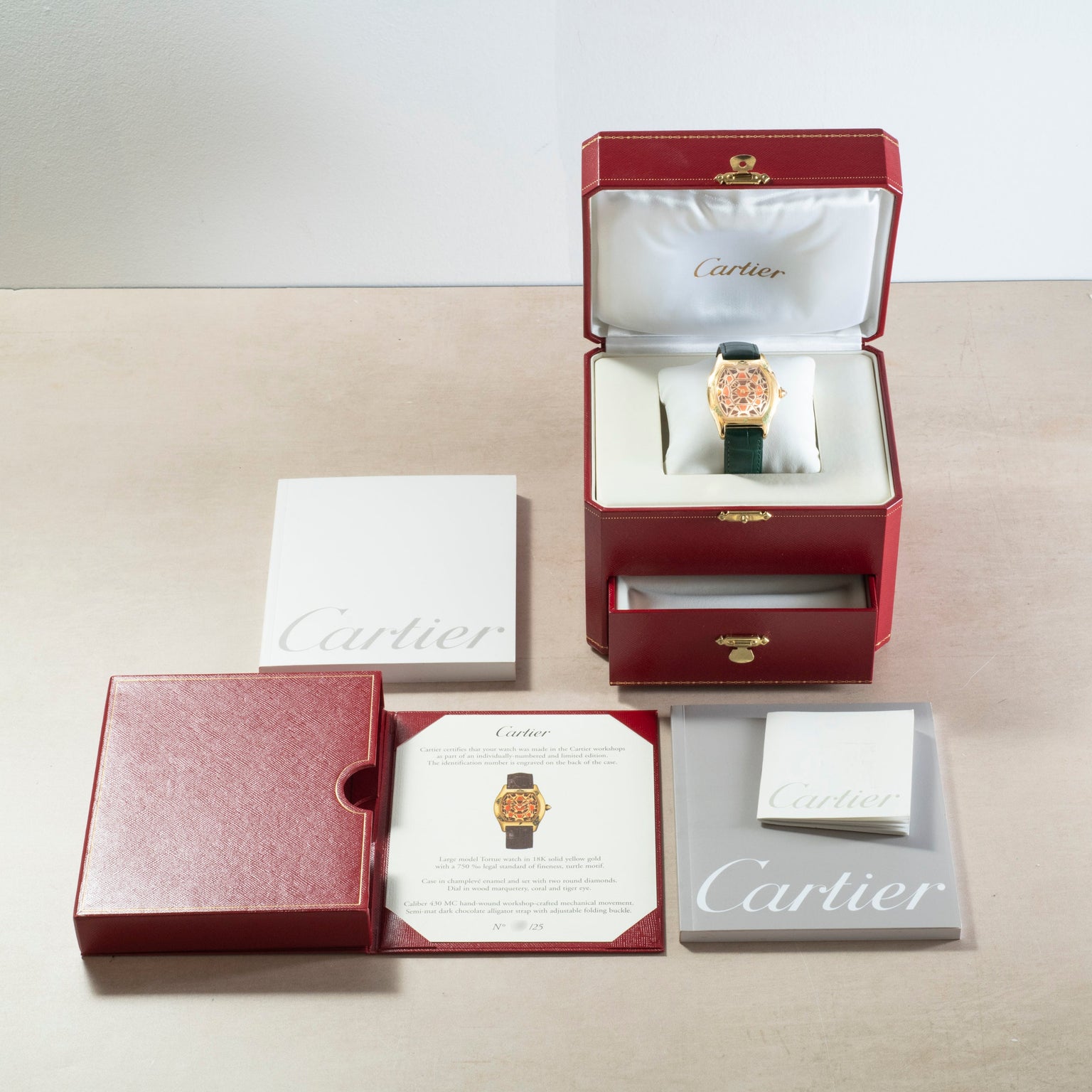 A Cartier Tortue XL Turtle Limited Edition watch in a red box, with documents, booklet, and outer case neatly arranged on a table.