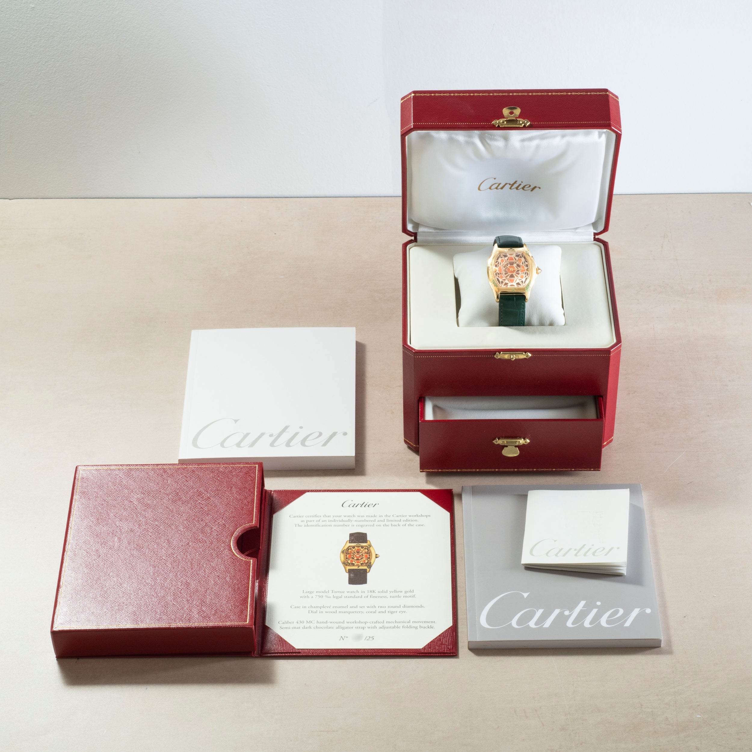 A Cartier Tortue XL Turtle Limited Edition watch in a red box, with documents, booklet, and outer case neatly arranged on a table.