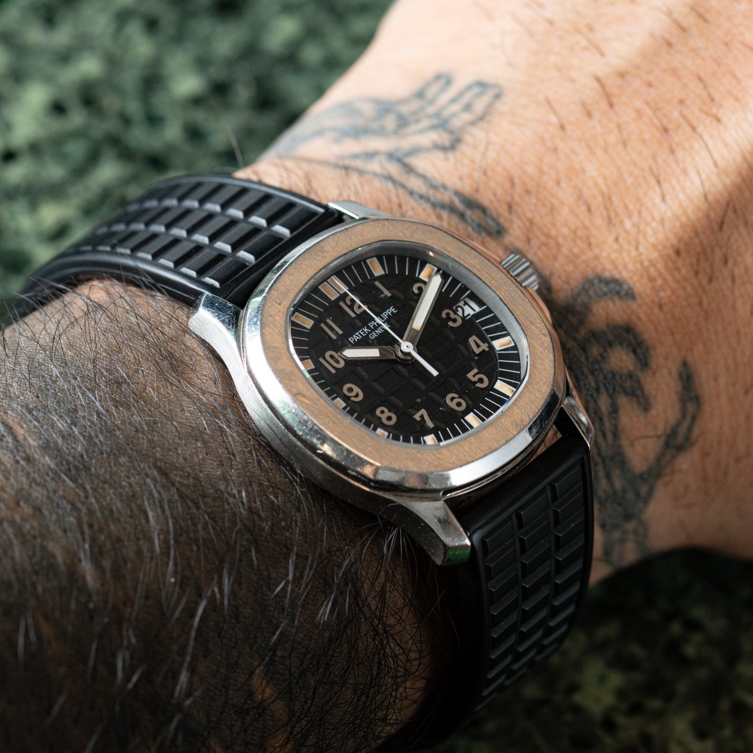 A wrist wearing the Patek Philippe Aquanaut with a black rubber strap and Arabic numerals, alongside a tattoo on the arm.