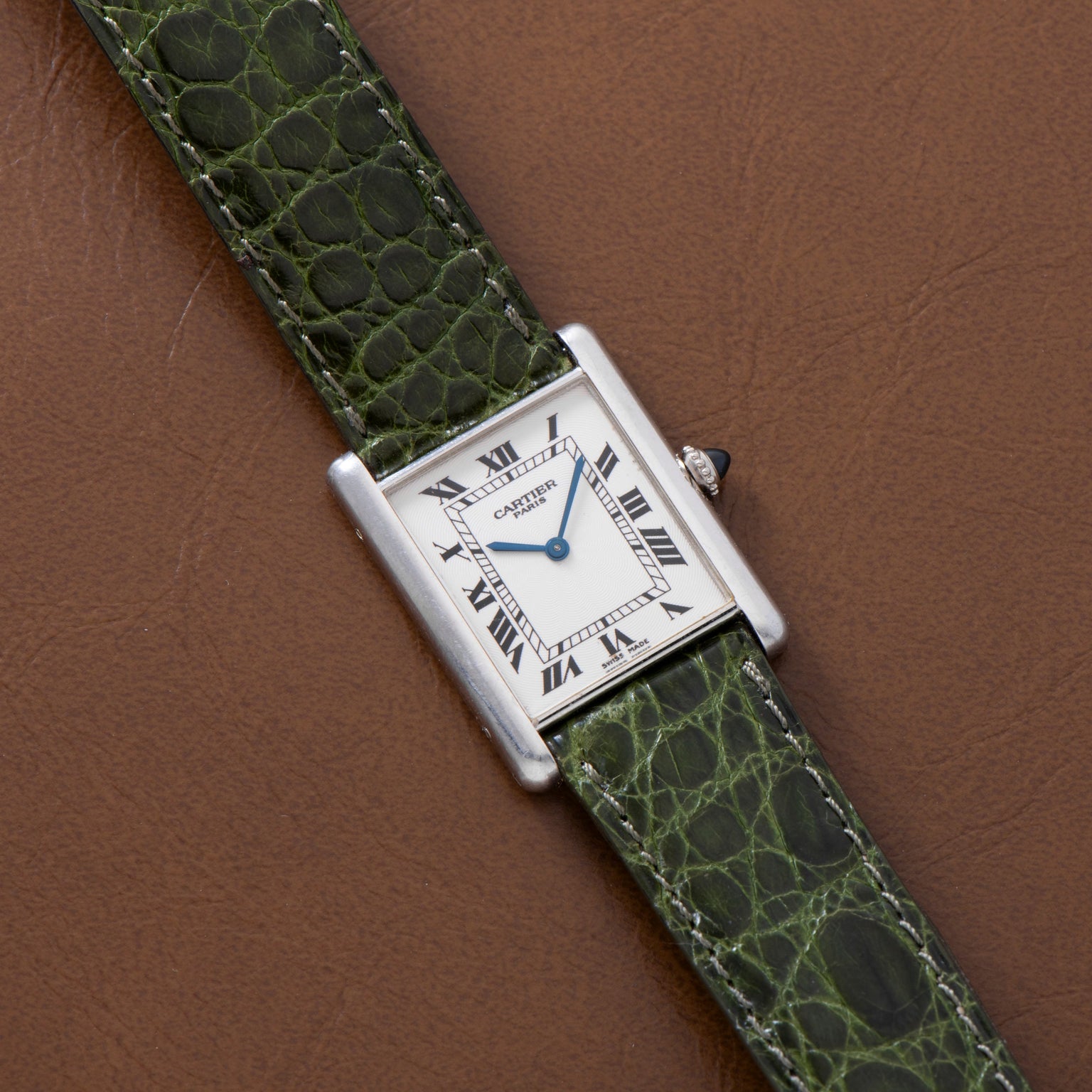 A Cartier Tank Louis CPCP watch with a green leather strap, displayed on a brown leather surface.