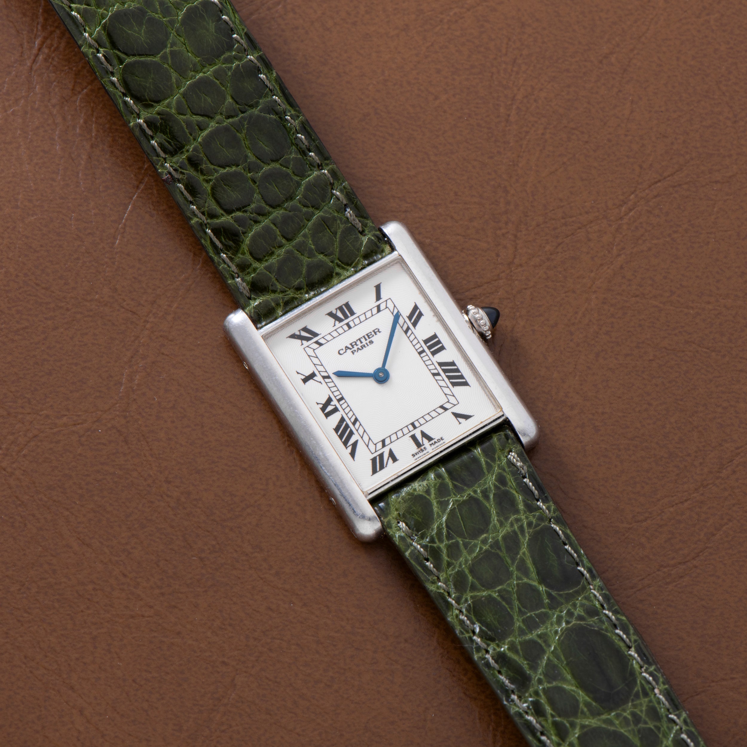 A Cartier Tank Louis CPCP watch with a green leather strap, displayed on a brown leather surface.