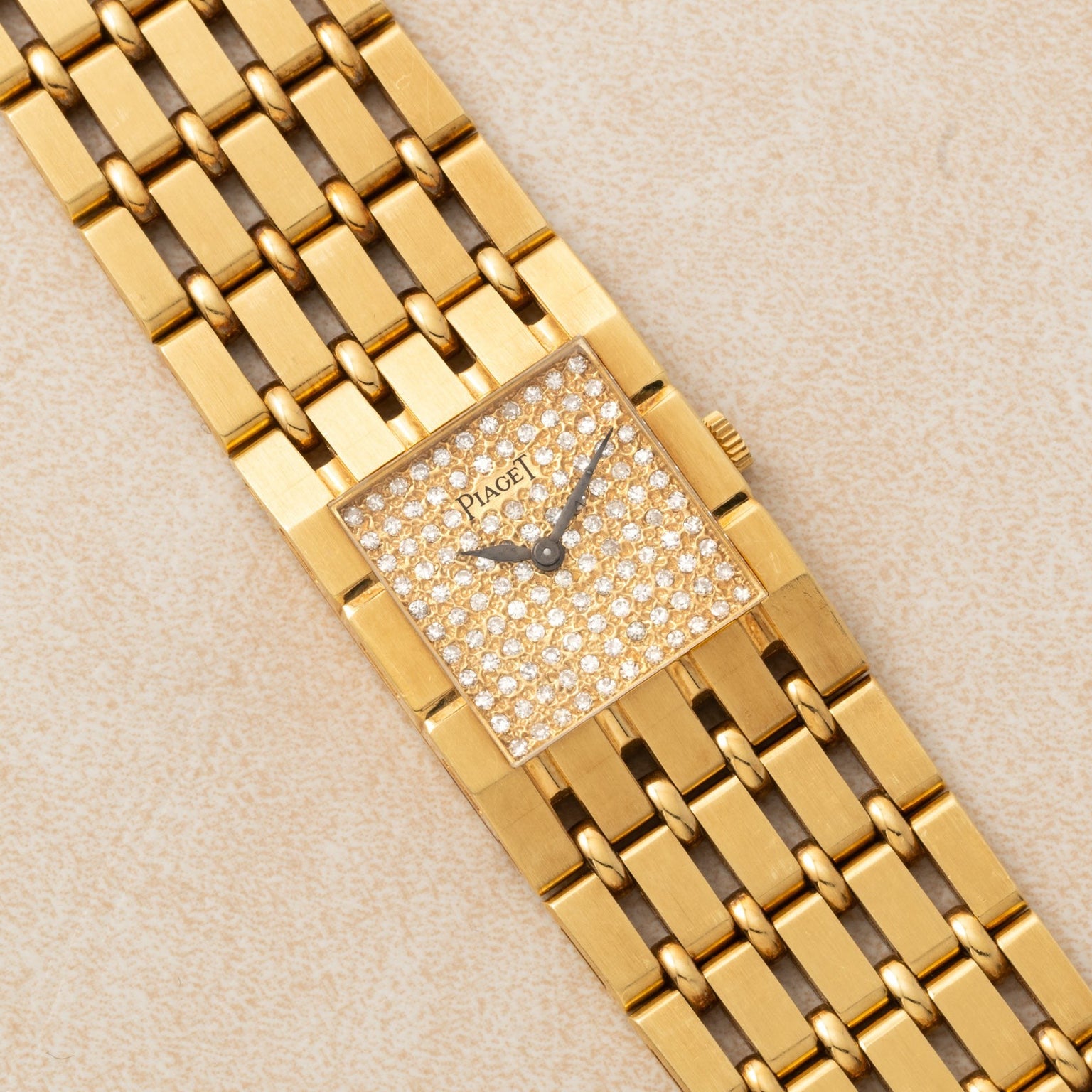 Piaget Dancer gold wristwatch featuring a rectangular, diamond-encrusted face and a linked gold bracelet, displayed on a beige surface.